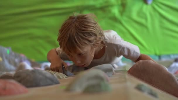 Ein kleiner Junge klettert in einer Boulderhalle die Wand hinauf — Stockvideo