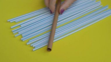 Renkli sarı arka planda birçok plastik pipetin el kamerasıyla yakın plan çekimleri. Bir insanın eli, plastiklerin üzerine bir bambu çubuğu koyuyor. Çevre dostu alternatif kavram