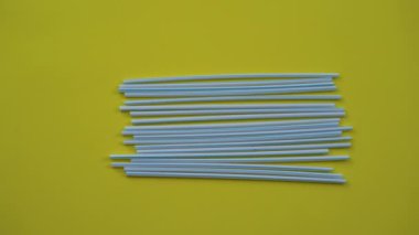Renkli sarı arka planda bir sürü plastik pipetin yakın plan çekimleri. Plastiklerin üzerine paslanmaz bir pipet koyan bir insan eli. Çevre dostu alternatif kavram