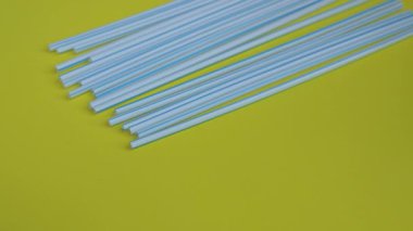 Renkli sarı arka planda bir sürü plastik pipetin el kamerasıyla yakın plan çekimleri. Bir insanın eli, plastiklerin üzerine kamış içen bir deste kağıt koydu. Çevre dostu alternatif
