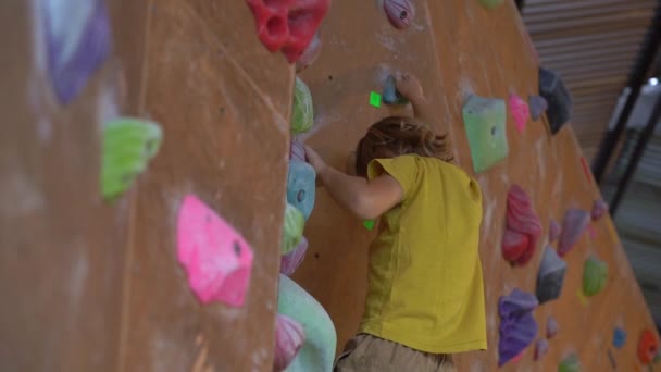 La toma en cámara lenta de un niño pequeño está escalando la pared en un gimnasio de escalada de rocas — Vídeo de stock