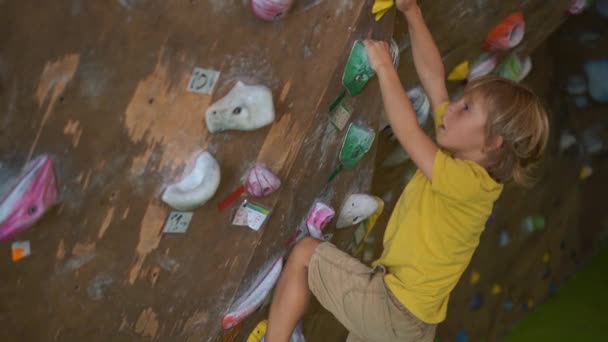 Медленный снимок маленького мальчика карабкается по стене в боулдеринговом спортзале — стоковое видео