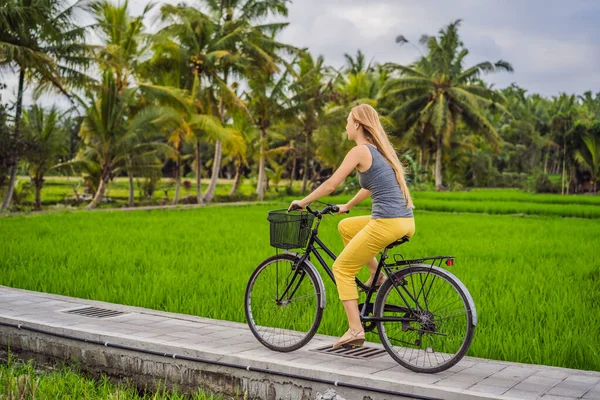 Genç bir kadın Ubud, Bali 'de pirinç tarlasında bisiklet sürüyor. Bali Seyahat Konsepti — Stok fotoğraf