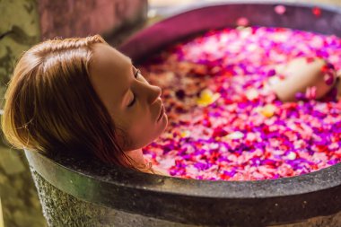 Tropik çiçekler ve aroma yağları yaprakları ile banyoda Çekici Genç kadın. Cilt gençleştirme için spa tedavileri. Spa salonunda çekici kadın. Kız çiçek yaprakları ile küvette rahatlatıcı. Lüks