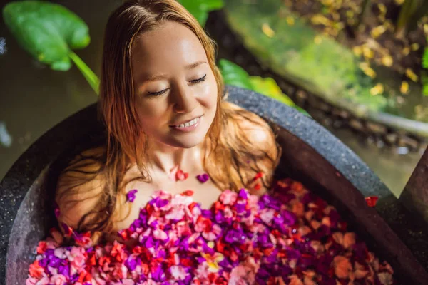 Mulher jovem atraente em banho com pétalas de flores tropicais e óleos de aroma. Tratamentos de spa para rejuvenescimento da pele. Uma mulher sedutora no salão de Spa. Menina relaxante na banheira com pétalas de flores. Luxo — Fotografia de Stock