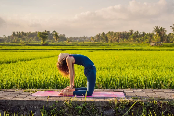 Junge Frau praktiziert Yoga im Freien in Reisfeldern am Morgen während eines Wellness-Retreats in Bali — Stockfoto