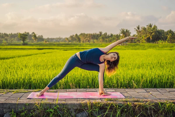 Fiatal nő gyakorlat jóga szabadtéri a rizs mezők a reggel folyamán wellness retreat Bali — Stock Fotó