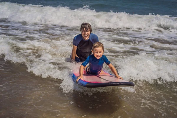 Padre o istruttore che insegna a suo figlio di 5 anni come navigare in mare in vacanza o in vacanza. Viaggio e sport con bambini concetto. Lezione di surf per bambini — Foto Stock