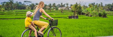 Anne ve oğlu Ubud, Bali 'de pirinç tarlasında bisiklet sürüyor. Çocuk konseptiyle Bali 'ye seyahat Banner, Uzun Format