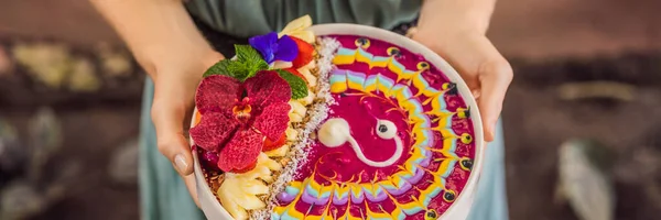 BANNER, LONG FORMAT Young woman having a medanean breakfast, eats Healthy tropical breakfast, smoothie bowl with tropical fruits, decorated with a pattern of colorful yogurt with turmeric and — стоковое фото