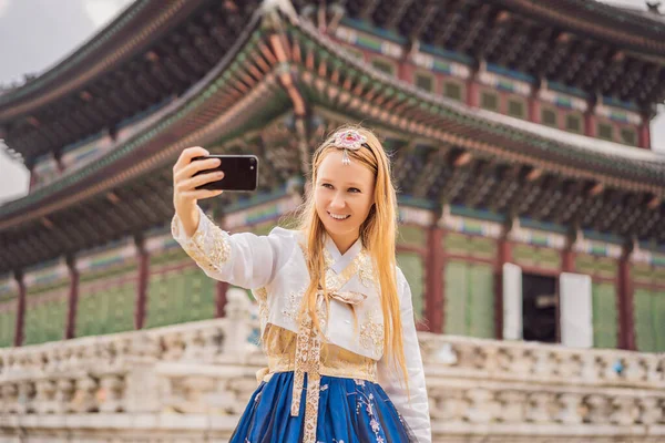 Fiatal kaukázusi női turista Hanbok nemzeti koreai ruhában a koreai palotában. Utazás Koreába koncepció. Nemzeti koreai ruhák. Szórakozás a turisták számára - nemzeti koreai ruhák kipróbálása — Stock Fotó