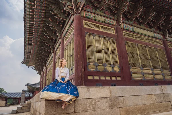 Young caucasian female tourist in hanbok national korean dress at Korean palace. Travel to Korea concept. National Korean clothing. Entertainment for tourists - trying on national Korean clothing