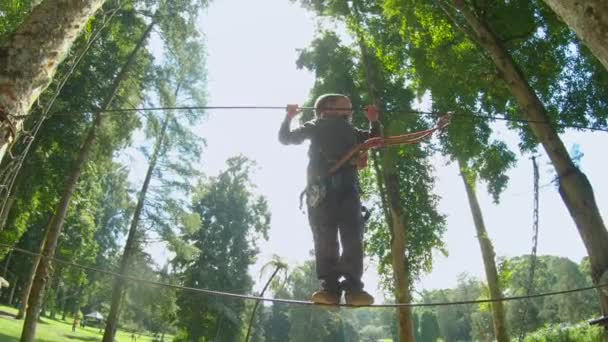 Экшн-камера, снятая двумя маленькими солдатиками в безопасности, которые забираются на маршрут в верхушках деревьев в лесном парке приключений — стоковое видео