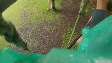 Orman macerası parkında ağaçların tepesine tırmanan emniyet kemeri takmış bir adamın görüntüsü. Yüksek ip izlerine tırmanıyor. Tırmanma faaliyetleri olan açık hava eğlence merkezi