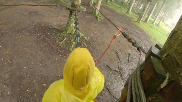 La cámara de acción de un niño pequeño con un arnés de seguridad sube a una ruta en las copas de los árboles en un parque de aventuras forestales. Se sube a un sendero de cuerda alta. Centro de diversiones al aire libre con actividades de escalada — Vídeos de Stock