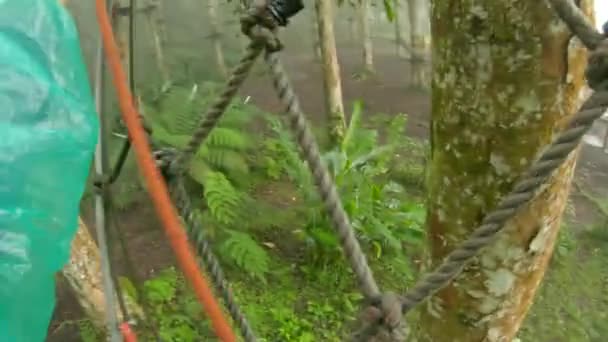 Точка зору постріл людини в запобіжному взутті, який піднімається по маршруту на деревах в лісовому парку пригод. Він піднімається по високій мотузці. Відкритий центр розваг зі скелелазінням — стокове відео