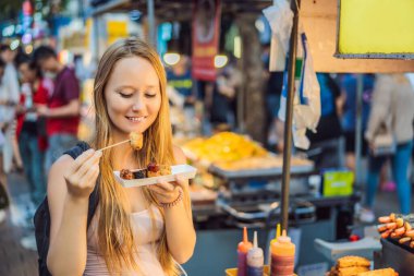 Genç bir turist Seul 'ün yürüyen bir caddesinde tipik Kore sokak yemekleri yiyor. Baharatlı fast food yerel Kore pazarında, Güney Kore 'de bulunur.