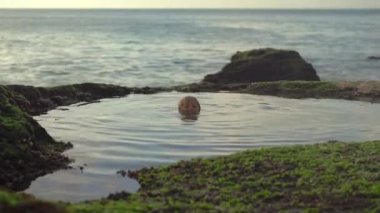 Küçük çocuk Bali adasındaki Pantai Tegal Wangi plajında deniz suyuyla dolu doğal bir gölette eğleniyor.