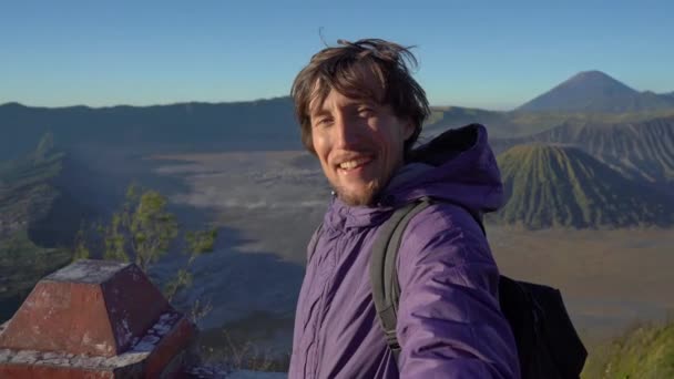 Um jovem blogueiro filma vídeo selfie no ponto de vista do vulcão Bromo dentro da caldeira Tengger na Ilha Java, Indonésia — Vídeo de Stock