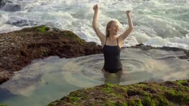 Genç bayan turist, Bali adasındaki Pantai Tegal Wangi plajında deniz suyuyla dolu doğal bir gölette eğleniyor.