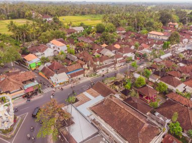 Bali 'de Ubud' da gökyüzünde tropik ağaçlar arasında kahverengi-turuncu kiremitli çatıları olan birçok villa var. Güneş üstlerinde parlıyor. Gökyüzü yatay fotoğrafı