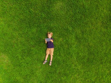 Parktaki çimlerin üzerinde yatan çocuk tablete bakıyor. Drone, quadracopter 'dan fotoğraflar