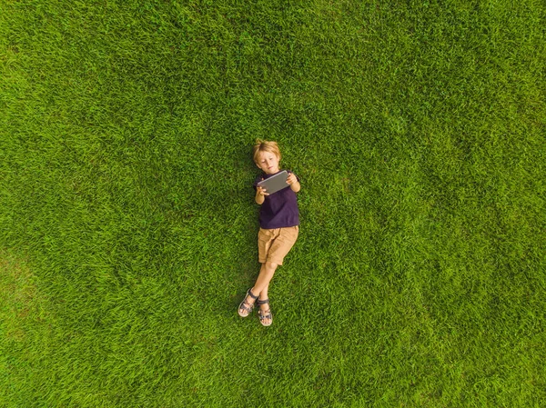 Rapaz deitado na relva do parque e olha para o tablet. Fotos do drone, quadracopter — Fotografia de Stock