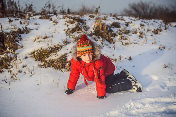 Chlapec v červených módních šatech hraje venku. Aktivní volný čas s dětmi v zimě v chladných dnech. Chlapec se baví s prvním sněhem. Happy little kid is playing in snow, good winter weather — Stock fotografie
