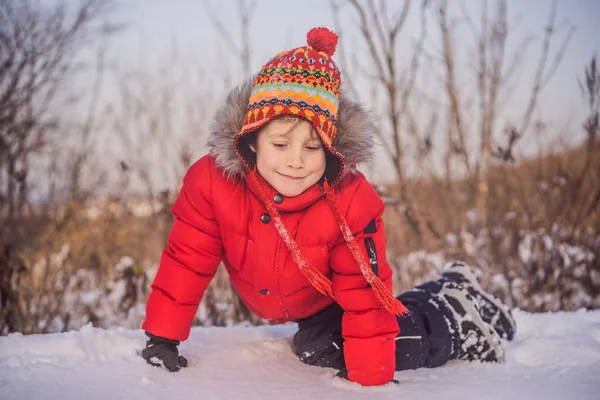 Boy in red fashion clothes playing outdoors. Active leisure with children in winter on cold days. Boy having fun with first snow. Happy little kid is playing in snow, good winter weather