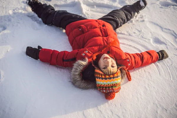 Un niño, un niño, yace en la nieve, hace un ángel de la nieve con sus brazos y piernas, emociones, risas — Foto de Stock