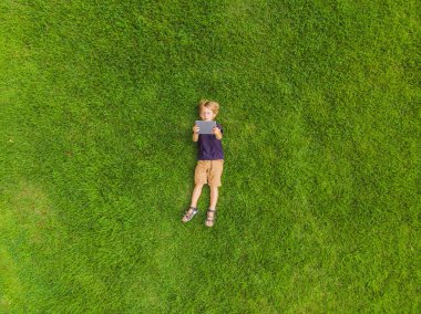 Parktaki çimlerin üzerinde yatan çocuk tablete bakıyor. Drone, quadracopter 'dan fotoğraflar