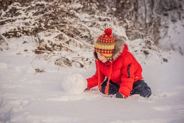 Lindo chico en ropa roja de invierno construye un muñeco de nieve. Invierno divertido concepto al aire libre — Foto de Stock