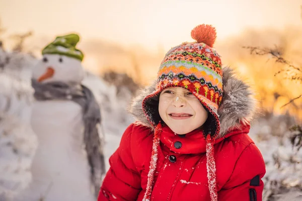 빨간 겨울 옷을 입은 귀여운 소년 이 눈 사람을 만든다. 겨울철 재미있는 야외 개념 — 스톡 사진