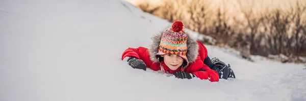 Boy in red fashion clothes playing outdoors. Active leisure with children in winter on cold days. Boy having fun with first snow. Happy little kid is playing in snow, good winter weather BANNER, LONG