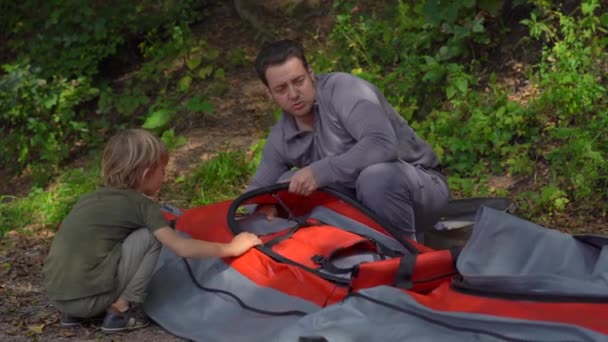 Un joven y su pequeño hijo en un lago o playa preparan un gran kayak inflable para nadar. — Vídeos de Stock