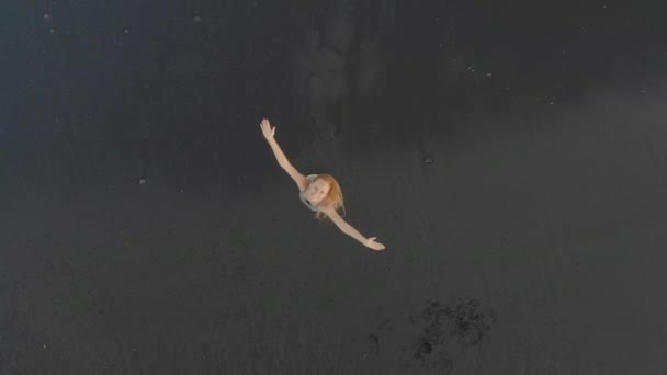 Luftaufnahme einer jungen Frau, die an einem Strand mit schwarzem Vulkansand spazieren geht und Spaß hat — Stockvideo