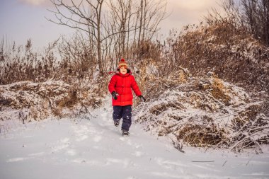 Kırmızı kışlık giysiler içindeki yakışıklı çocuk karda eğleniyor. Kış Eğlencesi Açık Hava Kavramları