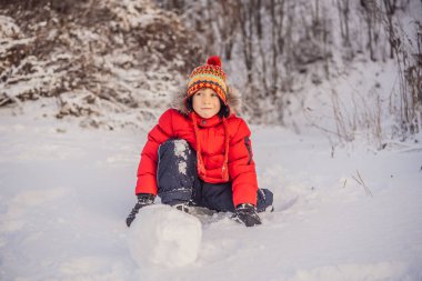 Kırmızı kışlık giysiler içindeki yakışıklı çocuk kardan adam yapıyor. Kış Eğlencesi Açık Hava Konsepti