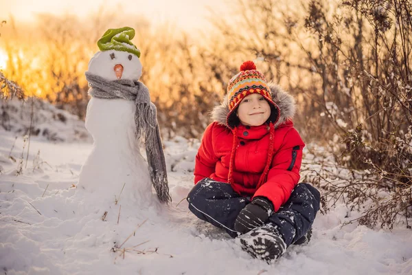 빨간 겨울 옷을 입은 귀여운 소년 이 눈 사람을 만든다. 겨울철 재미있는 야외 개념 — 스톡 사진