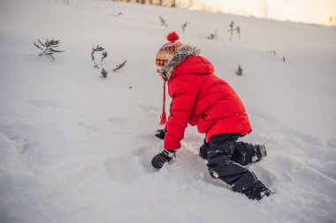 Kırmızı elbiseli çocuk dışarıda oynuyor. Soğuk günlerde kışın çocuklarla aktif bir eğlence. Çocuk ilk karla eğleniyor. Mutlu küçük çocuk karda oynuyor, güzel kış havası