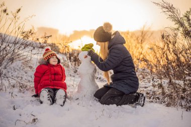 Mutlu aile sıcak giysiler içinde. Gülümseyen anne ve oğlu bir kardan adam açık yapma. Kış aktiviteleri kavramı