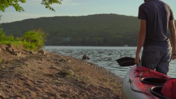 Молодий чоловік і жінка туристи несуть великий надувний каяк на березі моря або озера — стокове відео