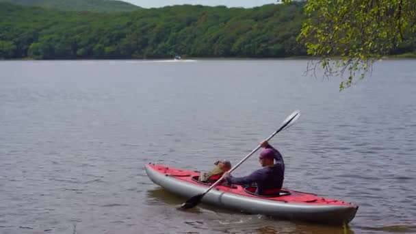 A young man and his little son in a big inflatable kayak paddle in a lake or bay — Stock Video