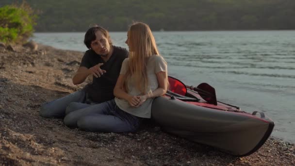 Un jeune homme et une jeune femme touristes assis près d'un grand kayak gonflable sur un bord de mer ou un lac — Video