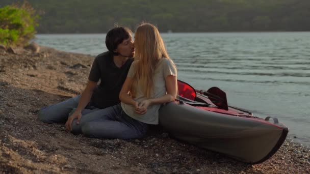 Mladý muž a žena turisté sedí u velké nafukovací kajak na pobřeží nebo jezera — Stock video