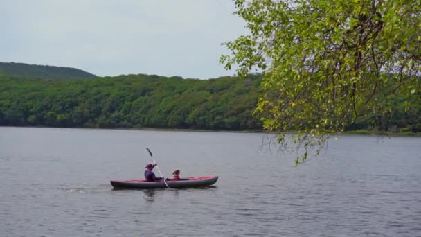 A young man and his little son in a big inflatable kayak paddle in a lake or bay — Stock Video