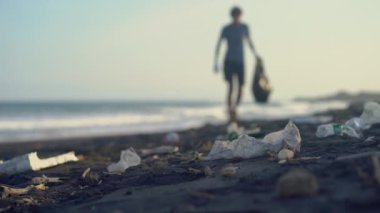 Genç adam bir çöpten plajı temizliyor.