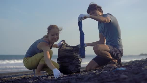 Молодая пара вычищает пляж от мусора — стоковое видео