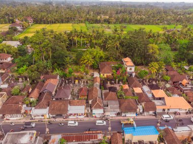 Bali 'de Ubud' da gökyüzünde tropik ağaçlar arasında kahverengi-turuncu kiremitli çatıları olan birçok villa var. Güneş üstlerinde parlıyor. Gökyüzü yatay fotoğrafı