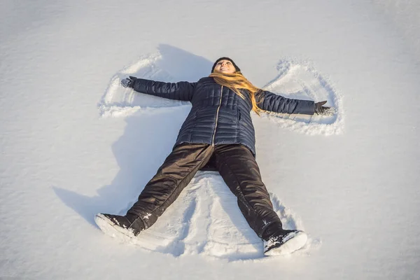 Woman warmly clothed in a cold winter forest makes snow angel figure at park. Copy space text